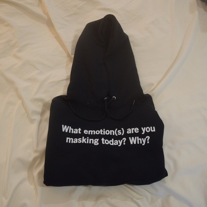 Może przedstawiać: Czarna bluza z kapturem z nadrukiem "What emotion(s) are you masking today? Why?" w kolorze białym na przodzie.
