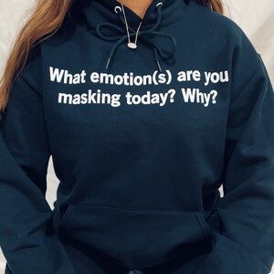 Może przedstawiać: Ciemnoniebieska bluza z kapturem z nadrukiem "What emotion(s) are you masking today? Why?" w kolorze białym.