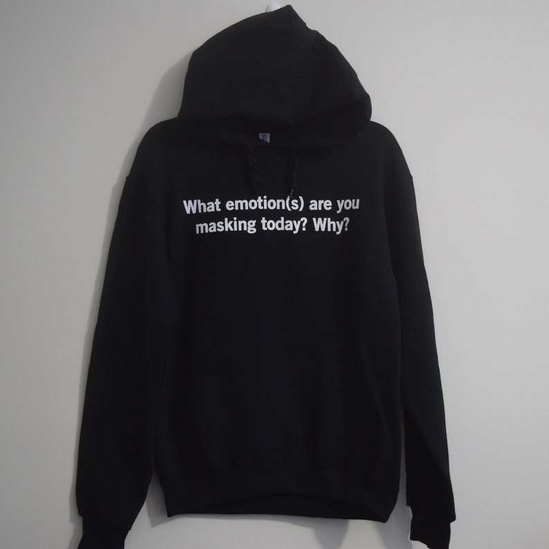 Może przedstawiać: Czarna bluza z kapturem z nadrukiem "What emotion(s) are you masking today? Why?" w kolorze białym na przodzie.