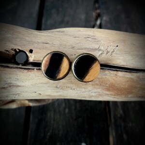 Peut inclure: Une paire de boucles d'oreilles rondes en bois avec des rayures noires et brunes. Les boucles d'oreilles ont un dos en métal doré.