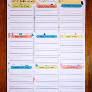 May include: A white Daily Brain Dump notepad with lined sections for notes. The notepad has colorful headers like "I need to do today," "Appointments," and "I need to call." The top has the text "Daily Brain Dump" and a space for the date.