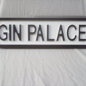 May include: A black and white sign with the words "GIN PALACE" in raised black letters.