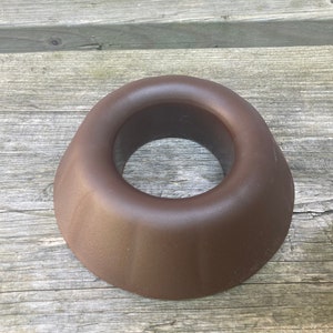 May include: A brown ceramic ring holder with a smooth, rounded surface. The holder is designed to hold a ring securely in place.