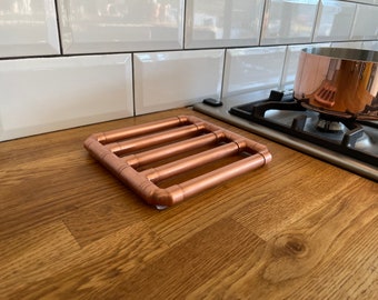 Salvamanteles de tubo de cobre con puntos de agarre de silicona incorporados.