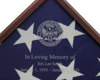 Könnte beinhalten: Eine amerikanische Flagge in einem Holzrahmen, die in Dreiecksform gefaltet ist. Die Flagge ist blau mit weißen Sternen und dem Siegel des US-Heeres. Der Text "In Loving Memory of Jim Lee Smith January 1, 1950 - January 2020" ist auf die Flagge gedruckt.