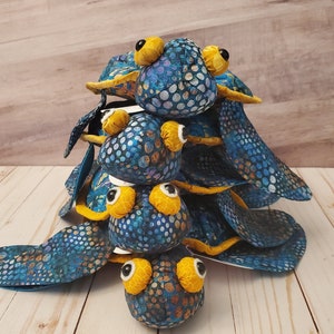 May include: A stack of four blue and yellow plush turtle toys with a speckled pattern. The turtles are stacked on top of each other with the largest turtle at the bottom and the smallest turtle at the top.