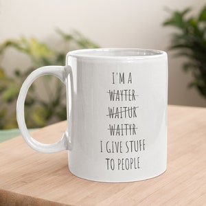 May include: White ceramic coffee mug with black text that reads "I'm a -waytter- -waitur- -waityr- I give stuff to people".