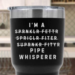 May include: Black stainless steel tumbler with a silver rim and lid. The tumbler has white text that reads "I'M A PIPE WHISPERER" with crossed-out words above. A humorous gift for a plumber or pipefitter.