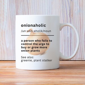 Puede incluir: Una taza de cerámica blanca con un gráfico de una cebolla marrón y la definición de diccionario de la palabra onionaholic, que describe a una persona que no puede controlar el impulso de comprar o cultivar más plantas de cebolla, con el texto see also greenie, plant stalker.