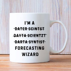 May include: White ceramic mug with a curved handle. The mug features the text "I'M A FORECASTING WIZARD" in a bold, black font. The words "DATER SCINTST", "DAYTA SCIENTZT", and "DARTA SYNTIST" are crossed out.