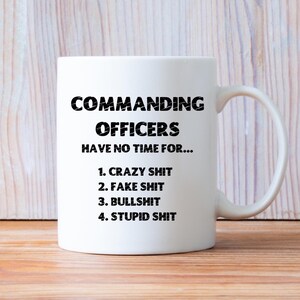May include: White ceramic mug with the text "COMMANDING OFFICERS HAVE NO TIME FOR..." followed by a list: "1. CRAZY SHIT, 2. FAKE SHIT, 3. BULLSHIT, 4. STUPID SHIT." The mug has a curved handle.