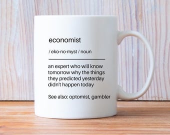 May include: A white ceramic mug featuring black printed text that defines the word economist as an expert who will know tomorrow why the things they predicted yesterday did not happen today, with the additional text see also: optimist, gambler.
