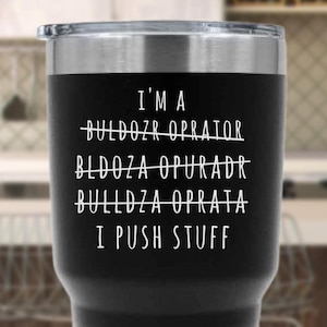 Peut inclure: Gobelet isotherme noir avec un couvercle argenté. Le gobelet porte l'inscription blanche "I'M A BULLDOZER OPERATOR I PUSH STUFF", avec des fautes d'orthographe barrées. Un cadeau humoristique pour les travailleurs du bâtiment.