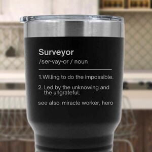 May include: A black stainless steel tumbler with a silver rim and lid. The tumbler features the word "Surveyor" with a definition, including "Willing to do the impossible." and "Led by the unknowing and the ungrateful."