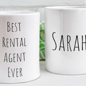 May include: Two white ceramic mugs. One mug says "Best Rental Agent Ever" and the other mug says "Sarah".
