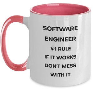 Pu&ograve; includere: Tazza da caff&egrave; in ceramica bianca con bordo e manico rosa. La tazza ha un testo nero che recita "SOFTWARE ENGINEER #1 RULE IF IT WORKS DON'T MESS WITH IT"