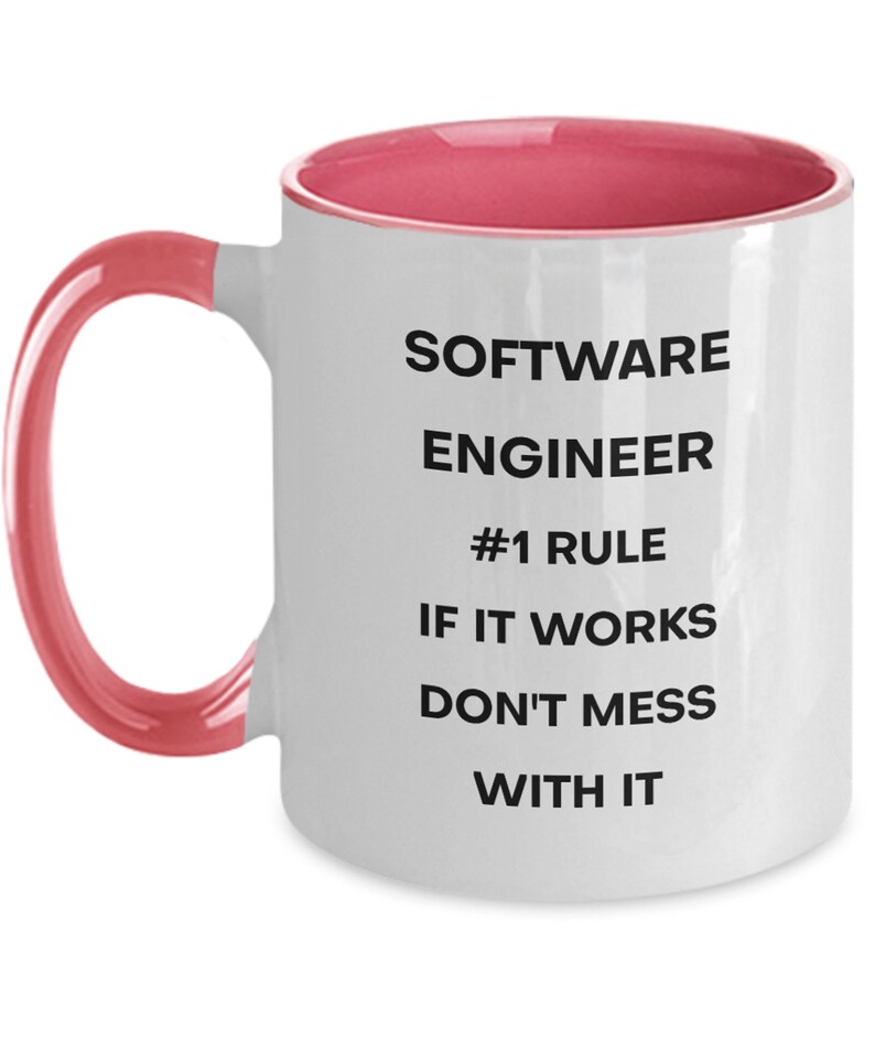 Pu&ograve; includere: Tazza da caff&egrave; in ceramica bianca con bordo e manico rosa. La tazza ha un testo nero che recita "SOFTWARE ENGINEER #1 RULE IF IT WORKS DON'T MESS WITH IT"