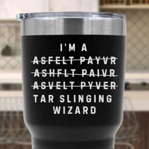 May include: Black insulated tumbler with a silver rim and lid. The tumbler features white text that reads "I'M A TAR SLINGING WIZARD" with crossed-out words above. A humorous gift for a construction worker.