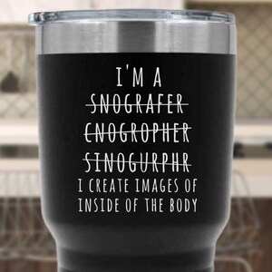 May include: Black stainless steel travel mug with white text that reads "I'm a Snografer, Enogropher, Sinogurphr. I create images of inside of the body."