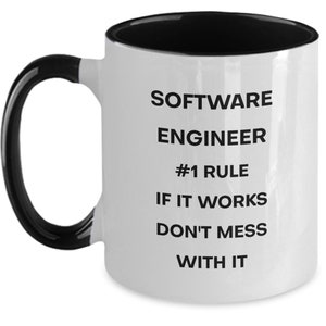 Pu&ograve; includere: Una tazza da caff&egrave; in ceramica bianca con interno e manico neri. La tazza ha un testo nero che recita "SOFTWARE ENGINEER #1 RULE IF IT WORKS DON'T MESS WITH IT"