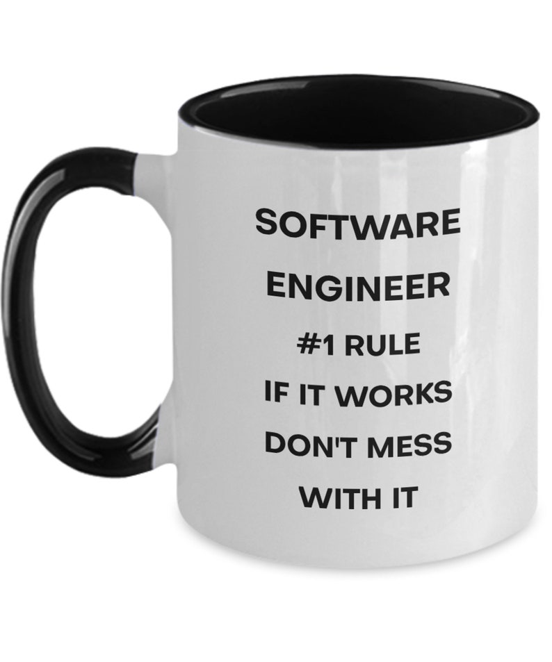 Pu&ograve; includere: Una tazza da caff&egrave; in ceramica bianca con interno e manico neri. La tazza ha un testo nero che recita "SOFTWARE ENGINEER #1 RULE IF IT WORKS DON'T MESS WITH IT"