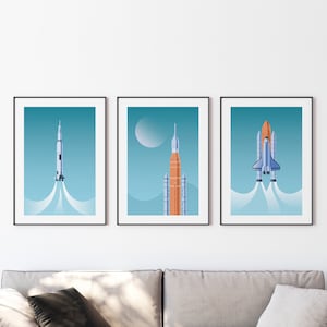 May include: Three framed prints of rockets launching into space. The first print features a white rocket with a blue and white flame. The second print features an orange rocket with a white flame. The third print features a blue and white space shuttle with a white flame.
