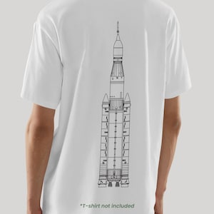 May include: White t-shirt featuring a black line drawing of a rocket on the back. The rocket design is detailed, showing the various stages and components. The bottom of the shirt has the text "*T-shirt not included" in green.
