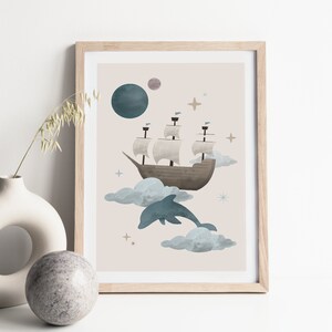 May include: A framed print featuring a whimsical illustration of a ship sailing on clouds with a dolphin leaping out of the water. The background is a light beige with stars and a blue planet.