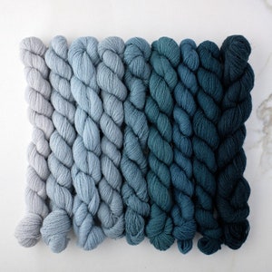 May include: A set of eight skeins of yarn in shades of blue, ranging from light gray to dark teal.