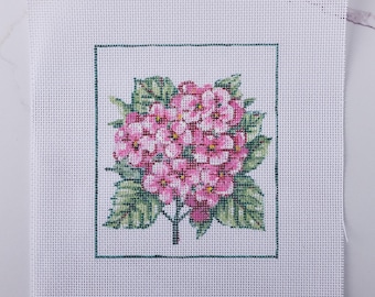 May include: Needlepoint canvas featuring a pink hydrangea flower design. The floral image is framed with a green border and set against a white background. The leaves are green, and the flower petals are pink.
