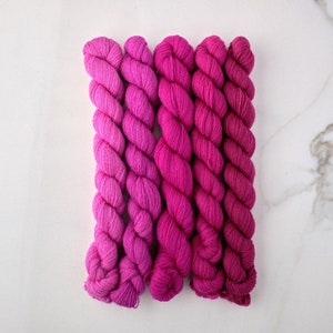 May include: Five skeins of pink yarn, each a slightly different shade, arranged in a gradient from light to dark.