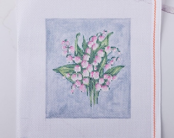 May include: A needlepoint canvas featuring a bouquet of pink lily of the valley flowers with green leaves against a light blue background. The canvas is white with an orange border on the right side. A color palette is visible at the bottom.