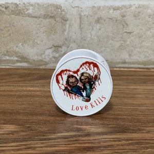 May include: White phone grip with a red heart design featuring two dolls holding weapons. The text "Love Kills" is printed below the heart.