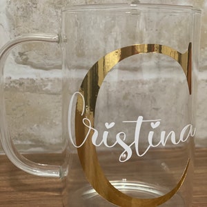 May include: A clear glass mug with a gold C and the name "Cristina" in white lettering.