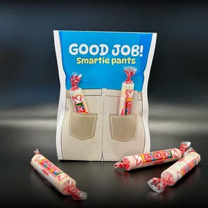 May include: A fun gift bag with a cartoon design of jeans and pockets. The bag is filled with Smarties sweets, with some peeking out of the pockets. The text "GOOD JOB! Smartie pants" is printed on the bag, a playful gift.