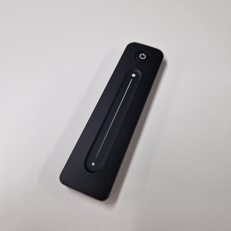 May include: A black remote control with a white power button and a white slider bar. The remote control is used to control lights.