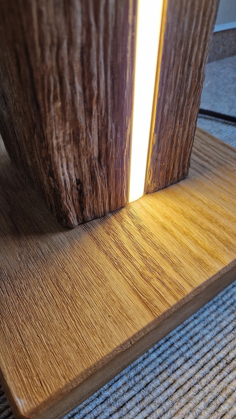 May include: A wooden lamp with a warm, natural wood finish. The lamp has a rectangular base and a tall, cylindrical body. A thin strip of LED light runs vertically down the center of the lamp, illuminating the wood grain.