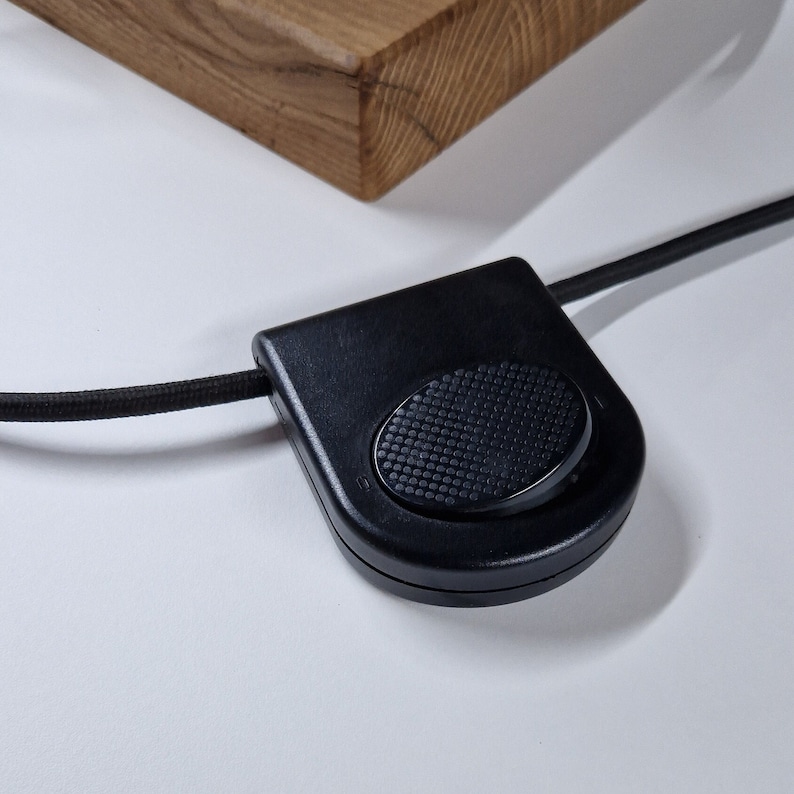 May include: A black foot switch with a round, textured button. The switch is connected to a black cord.
