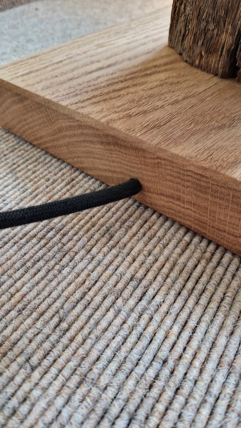 May include: A wooden lamp base with a black cord. The base is made of natural wood and has a rustic look. The cord is wrapped in black fabric.