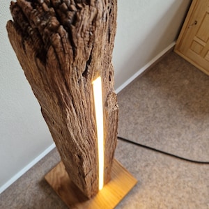 May include: A wooden floor lamp with a natural wood base and a long, thin, white LED light strip running vertically through the center of the wood.