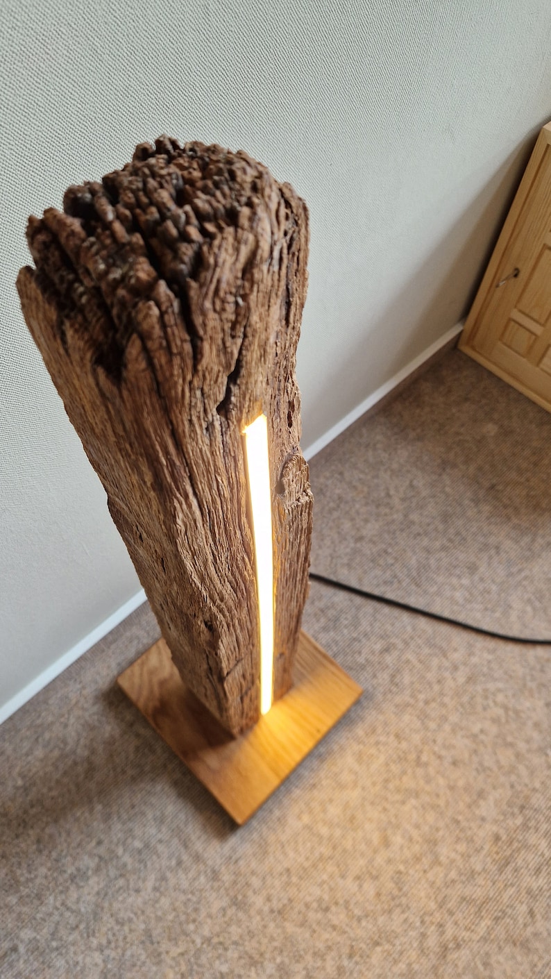 May include: A wooden floor lamp with a natural wood base and a long, thin, white LED light strip running vertically through the center of the wood.