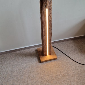 May include: A wooden floor lamp with a natural wood base and a long, thin, white LED light strip running vertically through the center of the wood.