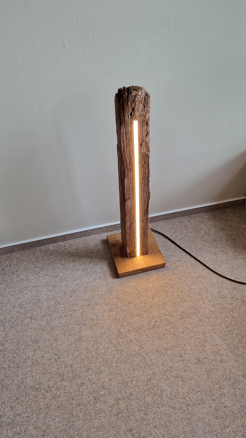 May include: A wooden floor lamp with a natural wood base and a long, thin, white LED light strip running vertically through the center of the wood.