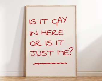 May include: A framed art print with the text "IS IT GAY IN HERE OR IS IT JUST ME?" in red handwritten style on a cream background. The frame is a light wood color, and the print is displayed on a wall above a wooden floor.