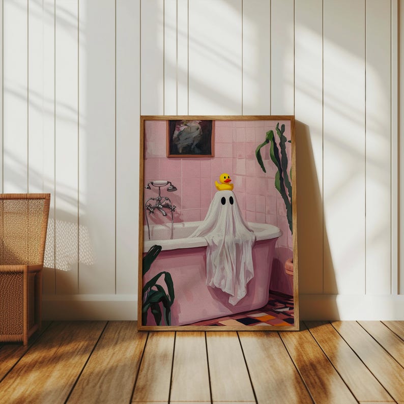 K&ouml;nnte beinhalten: Gerahmter Kunstdruck, der einen Geist in einer rosa Badewanne mit einer gelben Quietscheente zeigt. Das Badezimmer ist rosa gefliest, mit einer Vintage-Armatur und einem Gem&auml;lde. Das Kunstwerk ist in einem Holzrahmen vor einer wei&szlig;en Wand.