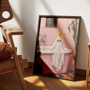 K&ouml;nnte beinhalten: Gerahmter Kunstdruck mit einer Illustration eines Geistes in einer Badewanne. Der Geist ist in ein wei&szlig;es Laken geh&uuml;llt und tr&auml;gt eine gelbe Quietscheente auf dem Kopf. Das Badezimmer ist rosa.