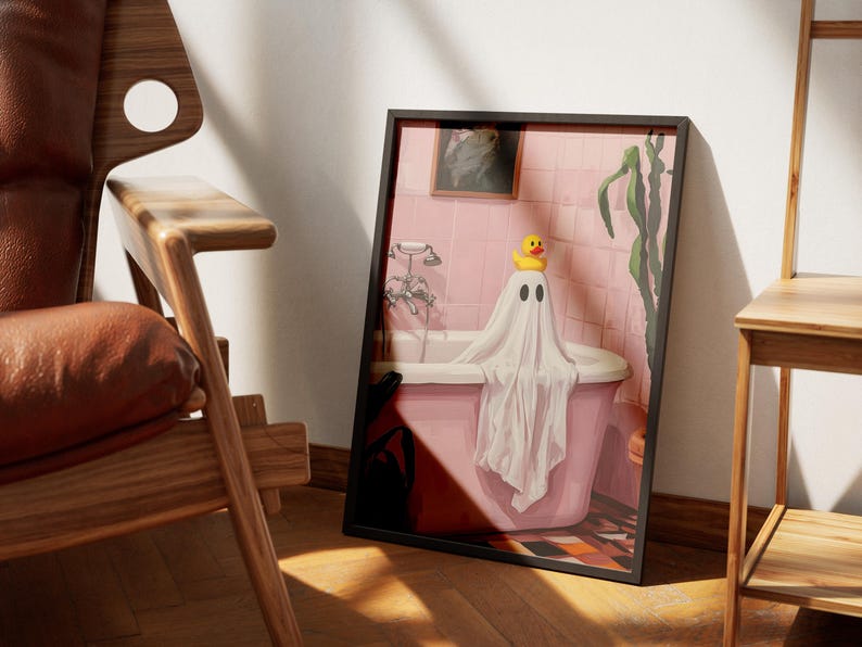 K&ouml;nnte beinhalten: Gerahmter Kunstdruck mit einer Illustration eines Geistes in einer Badewanne. Der Geist ist in ein wei&szlig;es Laken geh&uuml;llt und tr&auml;gt eine gelbe Quietscheente auf dem Kopf. Das Badezimmer ist rosa.