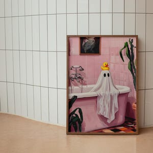 K&ouml;nnte beinhalten: Ein gerahmtes Kunstwerk zeigt eine rosa Badeszene mit einer Geisterfigur in einer Badewanne. Eine gelbe Quietscheente sitzt auf dem Kopf des Geistes. Das Kunstwerk ist vor einer wei&szlig; gefliesten Wand und einem hellbraunen Boden platziert.