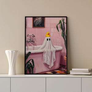K&ouml;nnte beinhalten: Ein gerahmter Kunstdruck zeigt einen Geist in einer Badewanne mit einer Gummiente auf dem Kopf. Das Badezimmer ist rosa, mit einem Gem&auml;lde an der Wand und einer Pflanze. Der Geist ist in ein wei&szlig;es Laken geh&uuml;llt.