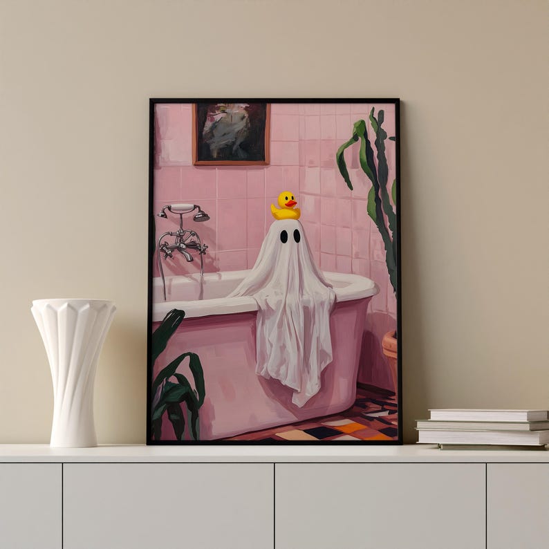 K&ouml;nnte beinhalten: Ein gerahmter Kunstdruck zeigt einen Geist in einer Badewanne mit einer Gummiente auf dem Kopf. Das Badezimmer ist rosa, mit einem Gem&auml;lde an der Wand und einer Pflanze. Der Geist ist in ein wei&szlig;es Laken geh&uuml;llt.